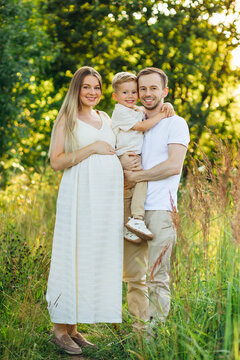 Pregnant mother and father holding their young son in a sunlit meadow family portrait