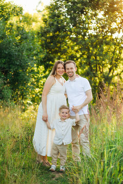 Young family portrait in a sunlit meadow: parents and toddler smiling outdoors in summer