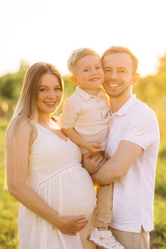 Happy young family portrait with pregnant mother, father and smiling little boy in golden sunlight