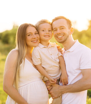 Smiling family portrait with pregnant mother, father and young son in golden hour outdoors