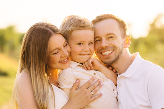 Happy young family embracing their son outdoors at golden hour, smiling parents and child together