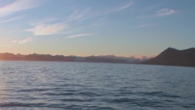 Arctic Ocean Ship Gliding Across Cold Polar Sea in Northern Seas. Snow-covered mountains remain visible beyond the cold open water and the distant polar horizon.