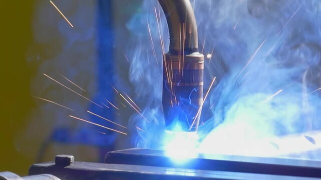 A precision argon welding robot joins metal pipes as the robotic arm follows the working area in an industrial setting. Bright sparks flare around the welding area as the process continues.