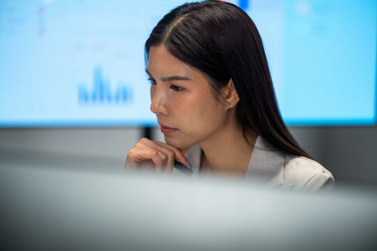  Attractive Asian businesswoman sitting in an office with deep concentration. A professional executive analysing financial graphs and researching company database information.