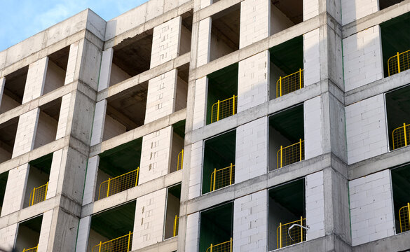 Construction site shows a building under development with empty windows and yellow safety railings