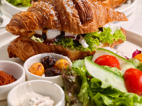 Breakfast croissant with salad and side dishes served on a white plate