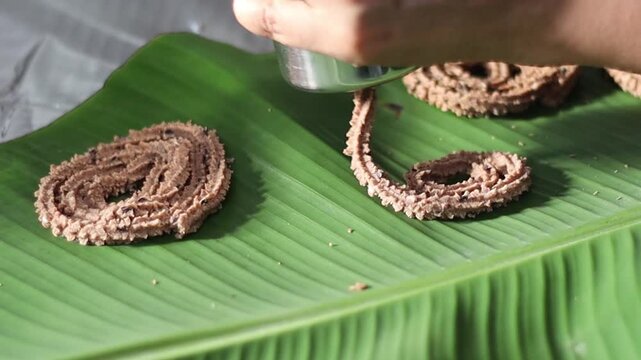 Pressing ragi dough through a murukku mould into spiral shapes on a plantain leaf