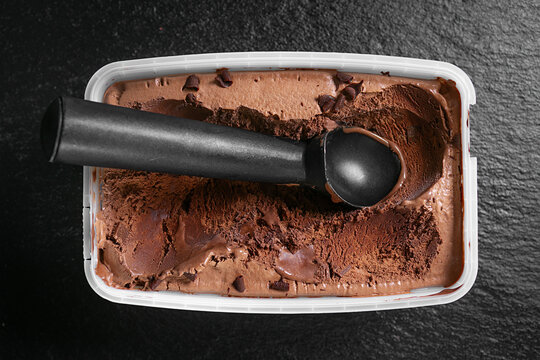 Chocolate ice cream with a scoop in a container.