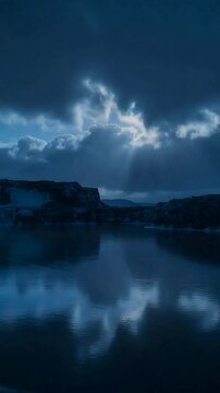 Vertical video: Shifting clouds exposing crescent moon, lighting reflection on calm lake near rocks