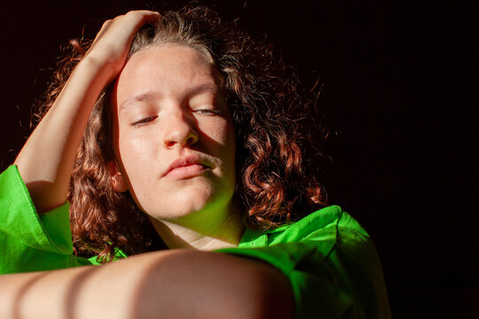Young person woman with subdued expression and hand in hair against dark background. Frustration and sadness. Negative emotions, stress and emotional wellbeing. Expressive portrait with copy space