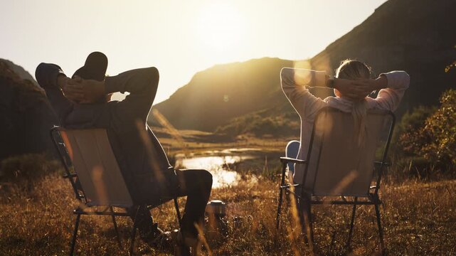Couple relax together in camping chairs, watch sunset over scenic mountain landscape, enjoy time in nature and an outdoor getaway focused on travel, connection, relaxation, escaping daily routine