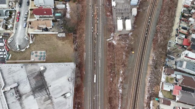 Aerial glide along railway tracks beside homes and parking lots. Parallel tracks divide residential blocks and parking areas while the camera moves along the transport corridor. Filmed in Queens NYC.