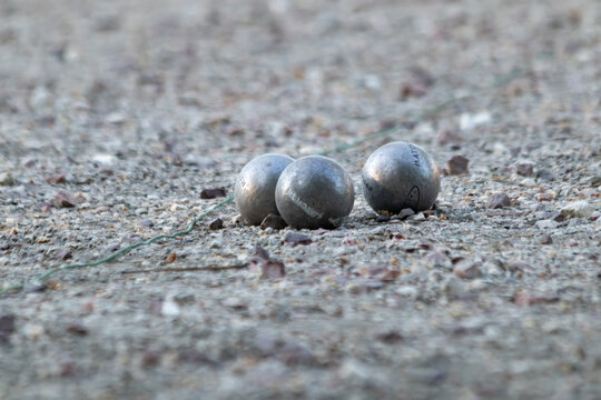 Three steel petanque boules on gravel ground, low angle ground level shot, soft bokeh background, outdoor leisure game in park, sunny day, string visible on ground, close up sport photography