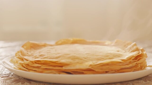Hot steam rises from stack of fresh homemade pancakes on white plate during detailed slow motion view. Cinematic morning breakfast video footage provides warm cozy asset for design element.