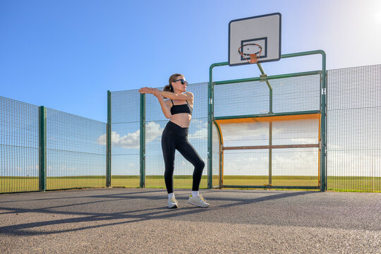 Woman doing an Arm Stretch on an Outdoor Basketball Court