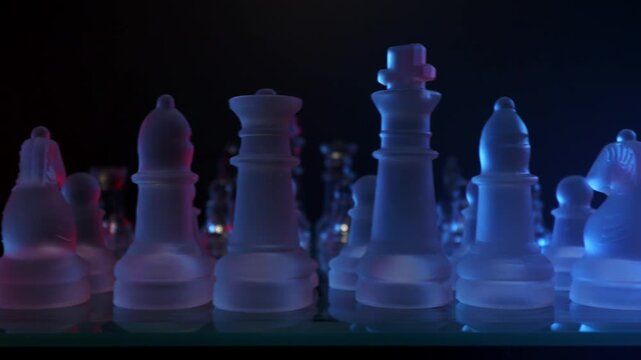 Close-up slider shot gliding past transparent glass chess pieces with dramatic red and blue lighting.