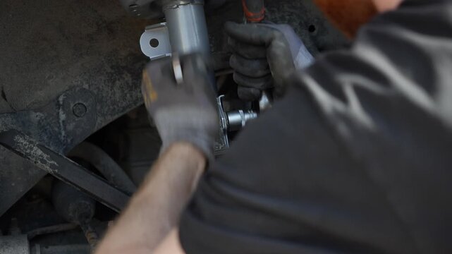 Mechanic hands in gloves tightening a bolt with a wrench tool while installing a new silver front suspension strut shock absorber into a car wheel well during a repair process. 