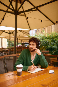Stylish young man enjoying a moment of creativity in a chic outdoor cafe