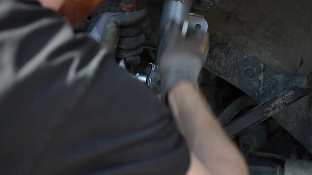 Mechanic hands in gloves tightening a bolt with a wrench tool while installing a new silver front suspension strut shock absorber into a car wheel well during a repair process. 