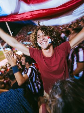 Paraguay football fan with smudged face paint cheering while holding a rippled flag in a crowded stadium, for sports and national pride