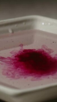 Vertical video: Dropping pipette sending pink droplets into white hex tray, mixing dye