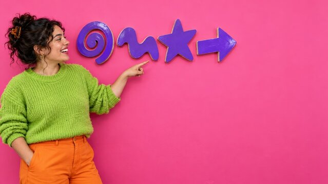 Wacky pomo design elements and a smiling woman in a lime green knit jumper pointing at a pink wall for creative banners and copy space