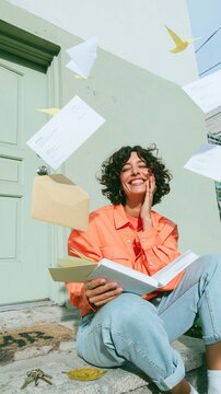 Middle Eastern woman laughing with an open envelope on a sunlit stone step, featuring floating papers for immigration and newcomer campaigns