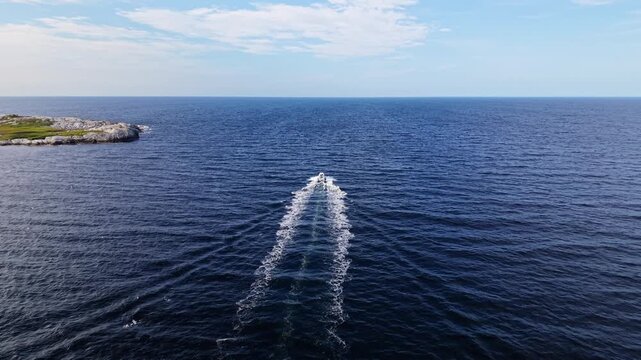 Aerial view of a white fishing boat with an outboard motor traveling at speed past the rocky shoreline of Prospect, Nova Scotia, with Atlantic waves surrounding the vessel.