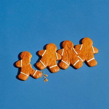Gingerbread man cookies with white icing in a row on a cobalt blue background, featuring one broken figure for food magazines and packaging