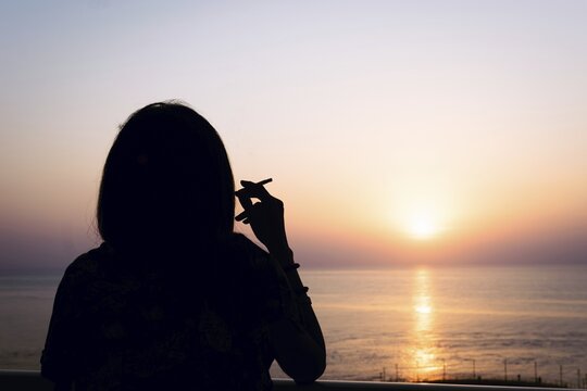 Silhouette of female person smoking cigarette with sea view horizon and sunset in the background. Batumi.Georgia