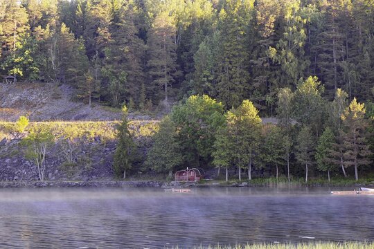 A quiet lake in morning fog, surrounded by thick forests, with a small wooden hut on the shore, Dals-Rostock, Dalsland Canal, Mellerud Municipality, Sweden