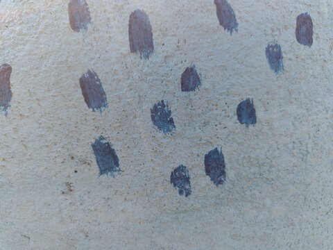 A textured beige concrete-like surface covered with scattered blue-gray oblong blotches that resemble fingerprints or thumbprints, arranged loosely across the cracked and grainy background.