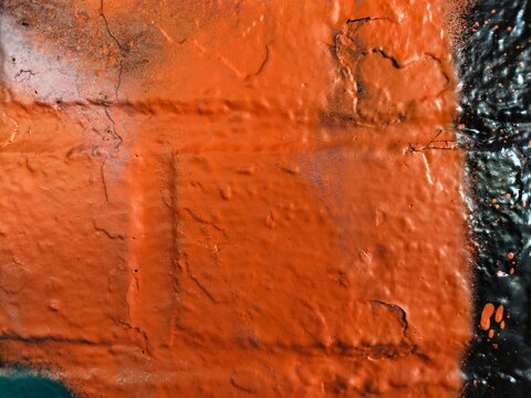 A close-up of an orange-painted brick wall with cracks, raised texture and a black painted edge on the right, showing thick layered paint and splatters.