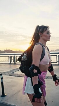 Sporty young woman rollerblades along city waterfront at sunset. Active female wearing backpack and protective gear enjoys peaceful evening ride on paved embankment path.