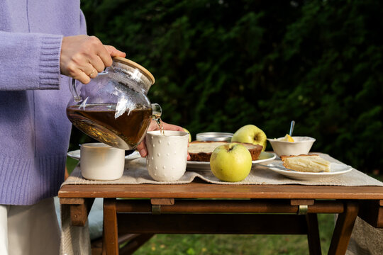 Woman pouring hot tea from glass teapot at garden table