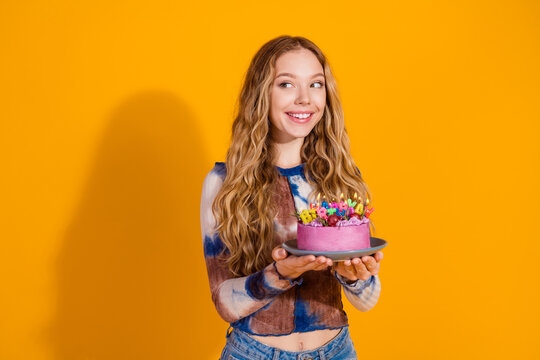Young girl with blonde hair presents pink birthday cake with candles against a bright yellow background