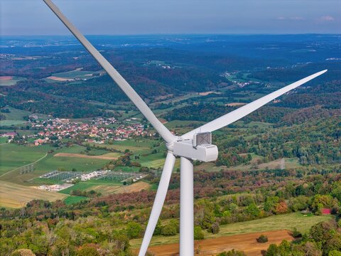 Aerial view of the Parc eolien du Lomont wind turbine overlooking rolling hills, green fields, and a small village in Vyt-les-Belvoir, Bourgogne-Franche-Comte, France.