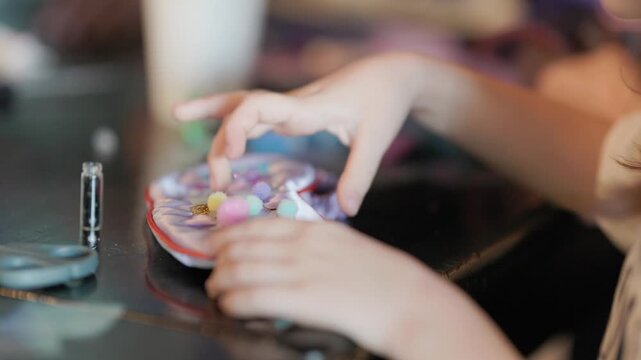 Creative girl's hands gluing colorful pom poms on a seashell pouch