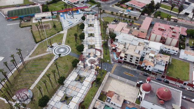 Aerial view of the public square in Callao featuring paved walkways, manicured lawns, palm trees, and nearby urban buildings in Callao, Callao Region, Peru.
