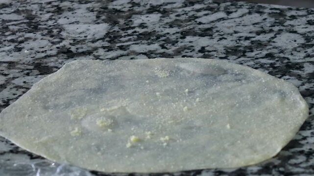 Hands spreading oiled msemen dough into thin sheet on counter