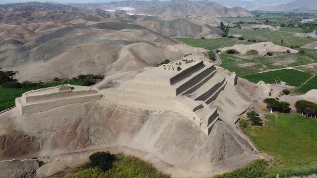 Aerial view of Fortress Paramonga, an ancient adobe structure set within a desert landscape with surrounding hills and agricultural fields in Paramonga, Peru.