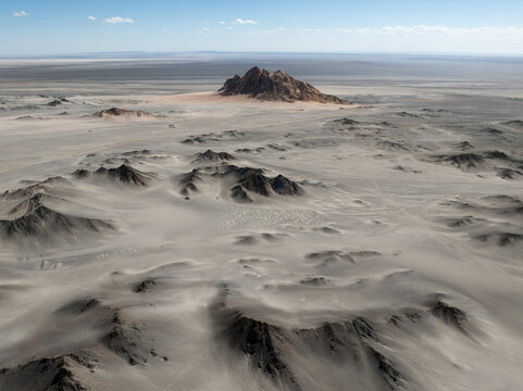 Aerial view of the arid desert landscape surrounding the rocky Heidushan mountain with sandy dunes and rolling hills, Haixi Mongol and Tibetan Autonomous Prefecture, Qinghai, China.