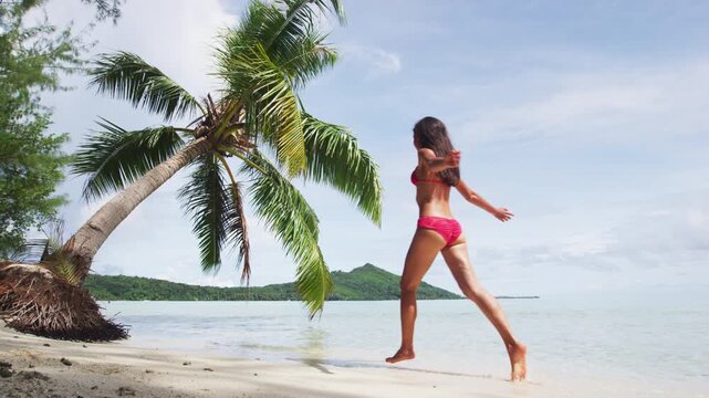 Happy young woman in red bikini running into water on beach. Cheerful female is enjoying nature during her summer vacation travel. Raw video of real woman without any makeup