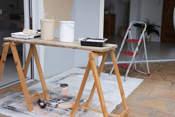 Sawhorses are holding plank bench with beige and white paint cans, red ladder on tiled patio © WavebreakMediaMicro