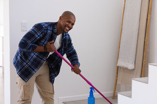 African American man cleaning home stair landing, shirt, tan pants, with pink mop