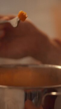 Inside a home kitchen, a man samples a forkful of pumpkin to check doneness for a vegetable stew, engaging in a culinary process for a traditional dinner following a gastronomy recipe