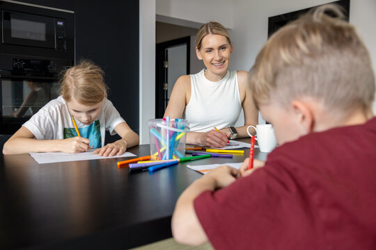 Mother with two children playing drawing game together at home. Quality time