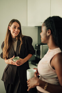 Diverse business women colleagues talking and smiling during office coffee break, networking in workplace kitchen
