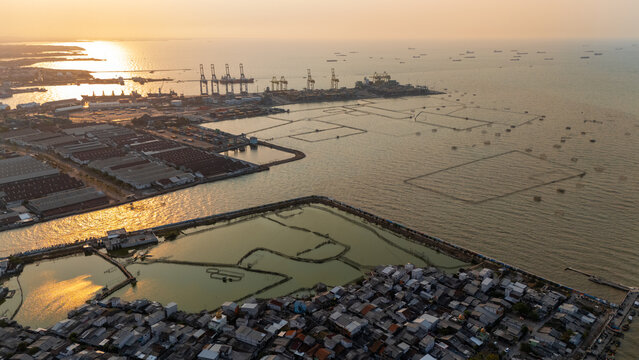 Aerial view of Pelabuhan Tanjung Emas port area with industrial facilities, shipping containers, and fish ponds along the coast at sunset in Semarang Utara, Central Java, Indonesia.