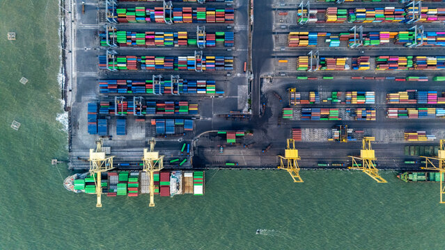 Aerial view of Pelabuhan Tanjung Emas with rows of colorful shipping containers, gantry cranes, and a cargo ship docked at the terminal in Semarang Utara, Central Java, Indonesia.